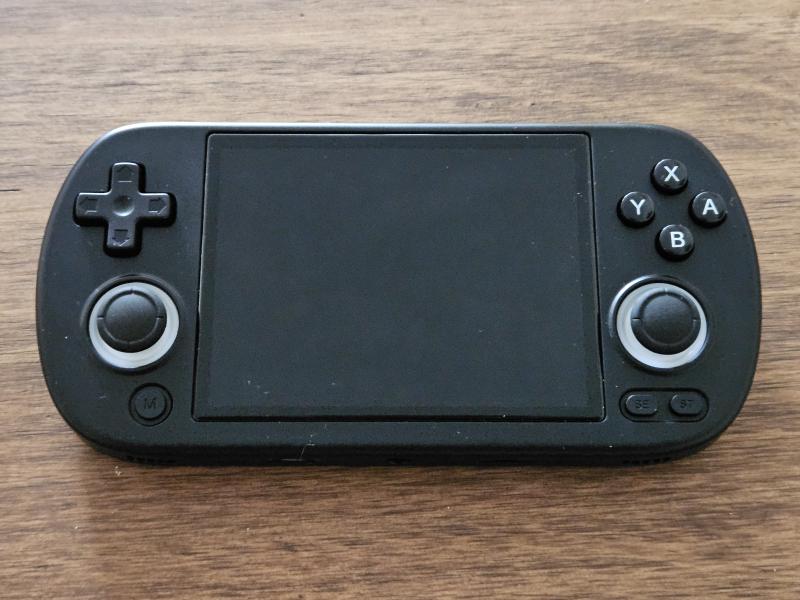 Console de jeu portable Anbernic RG40XX H, au format horizontal, photographiée de dessus sur une table en bois, écran éteint.