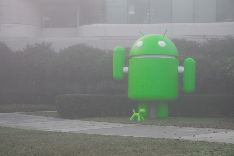 Statue géante du robot vert d’Android devant un bâtiment du siège de Google à Mountain View, dans le brouillard.