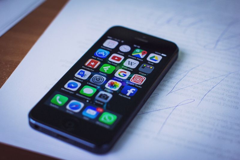 Un iPhone posé sur une feuille, écran allumé : une grille d'icônes d'applications, dont celle de l'App Store.