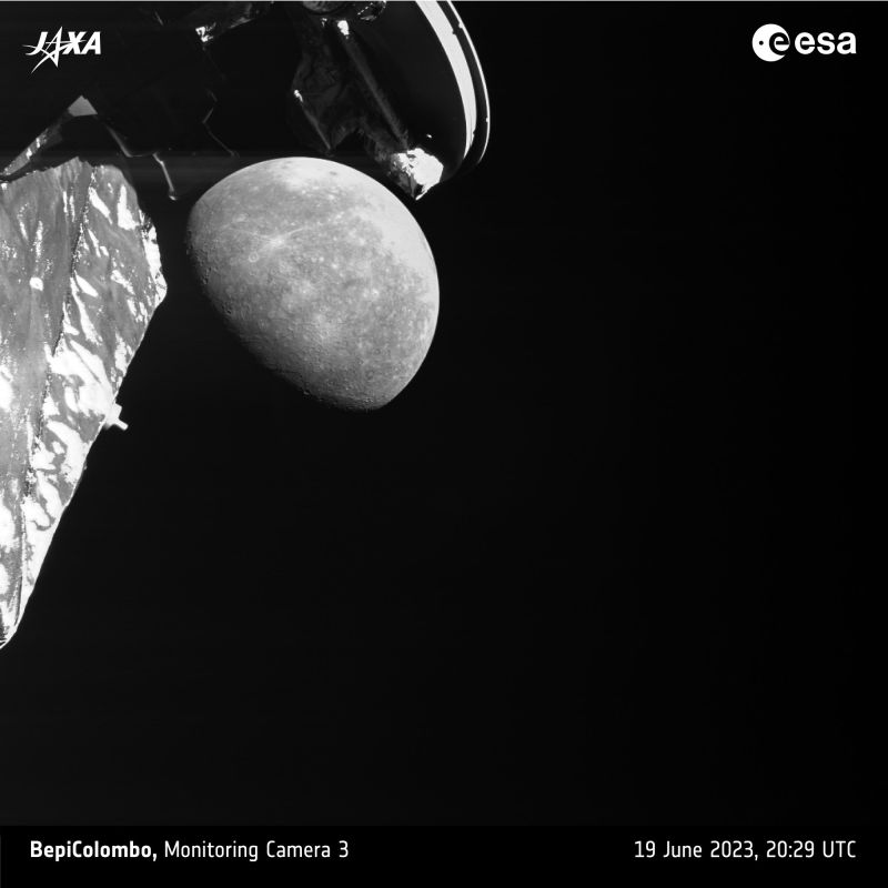 Photo en noir et blanc prise par une caméra de surveillance de BepiColombo : Mercure, à moitié éclairée et criblée de cratères, apparaît sur fond noir, encadrée par des éléments de la sonde au premier plan, dont l’arrière d’une antenne en haut.