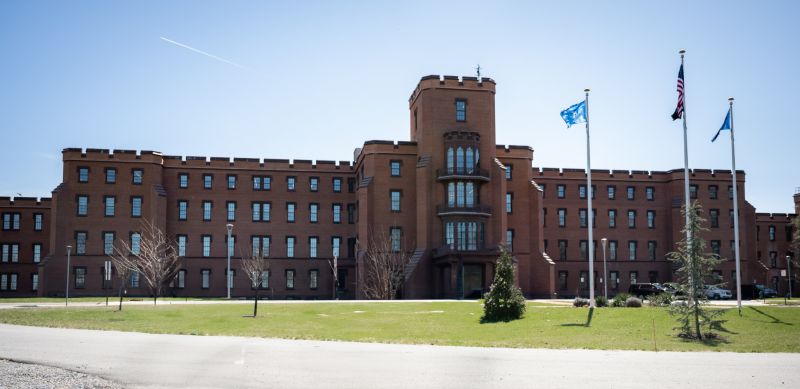 Siège du ministère américain de la Sécurité intérieure à Washington : un grand bâtiment de brique à créneaux et tour centrale, devant une pelouse et trois mâts portant des drapeaux, sous un ciel bleu.