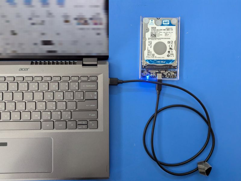 Un disque dur relié par un câble USB-C à un ordinateur portable posé sur une table bleue.