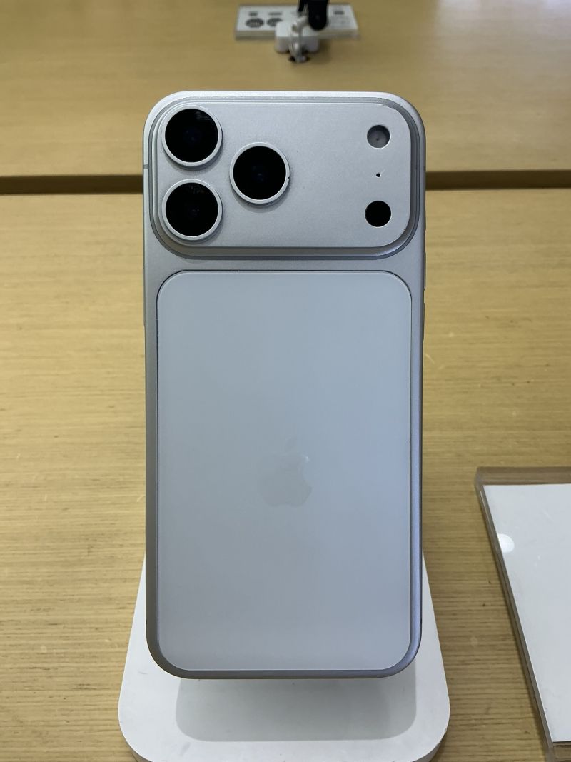 Dos d'un iPhone blanc argenté debout sur un présentoir de magasin, avec en haut son bloc photo à trois objectifs, un flash et un capteur.