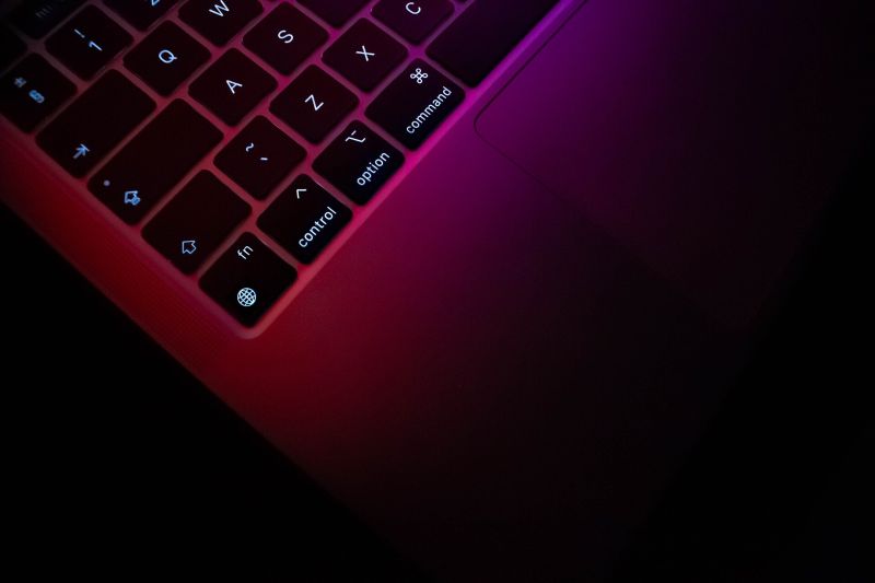 Gros plan sur le clavier rétroéclairé d’un MacBook Pro, touches command, option et control, sous une lumière rose et violette.
