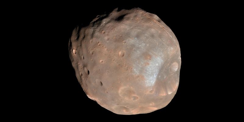 Phobos, lune de forme irrégulière, brun-rouge et criblée de cratères, éclairée sur fond noir ; un grand cratère au bord bleuté occupe sa partie inférieure droite.