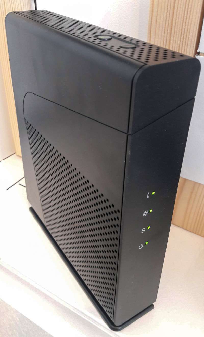 Box internet noire posée à la verticale, façade percée d'une grille d'aération, quatre voyants verts sur la tranche et deux boutons sur le dessus.