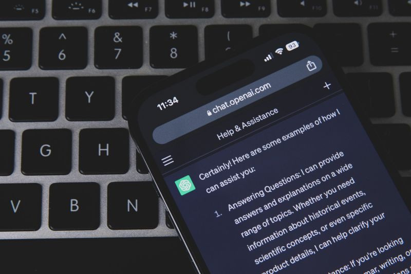 Un smartphone posé sur un clavier d'ordinateur affiche une réponse de ChatGPT dans son navigateur, sur le site chat.openai.com.