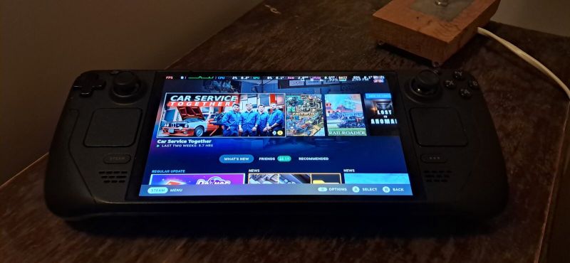 Console portable Steam Deck OLED posée sur une table, écran allumé sur l'écran d'accueil de la console, qui affiche les jeux récemment lancés.