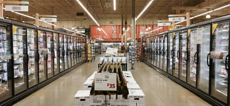 Allée de supermarché bordée de part et d'autre de meubles réfrigérés à portes vitrées, remplis de produits surgelés.