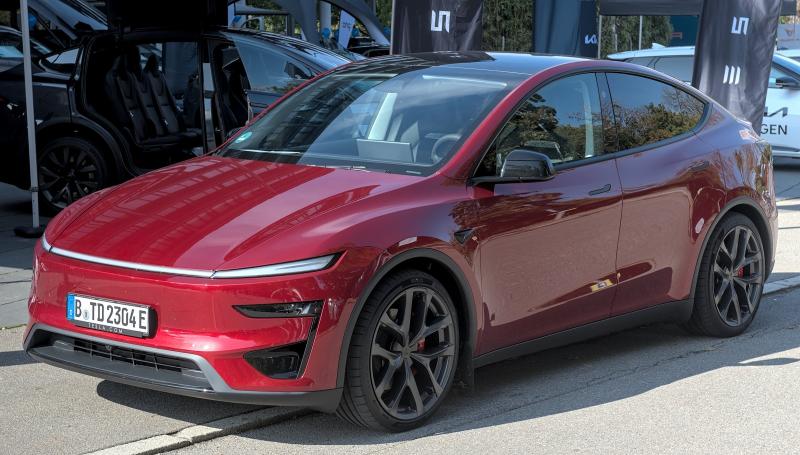 Un SUV électrique Tesla Model Y rouge, vu de trois quarts avant, garé sur un stand en plein air.
